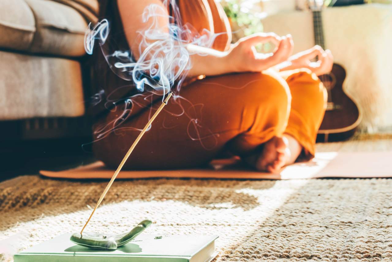 evde bir odanın içerisinde tütsü ve mumlarla dolu bir alanda meditasyon yapan kadın