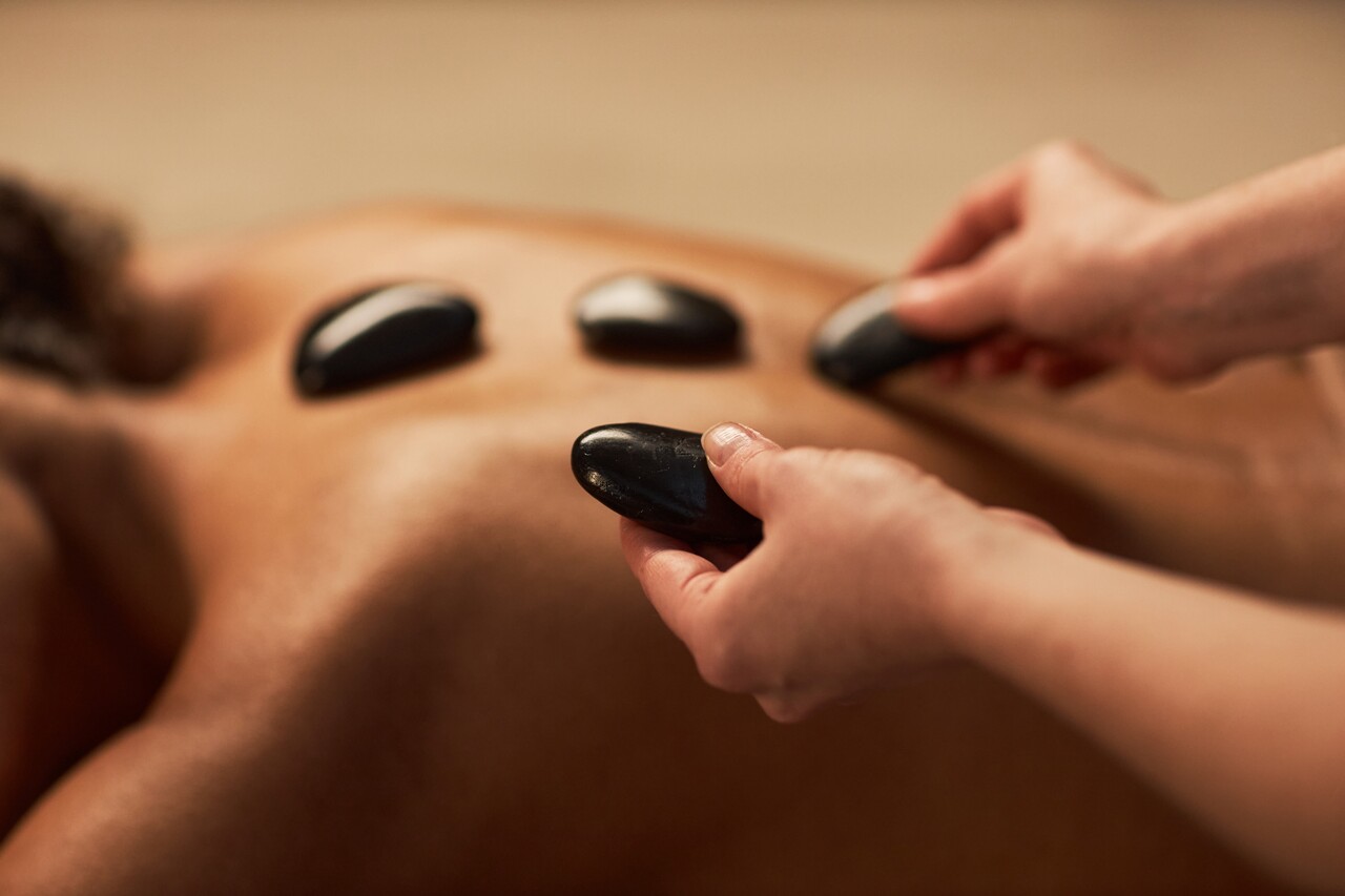 a hot stone massage expert placing the stones on the back of a woman