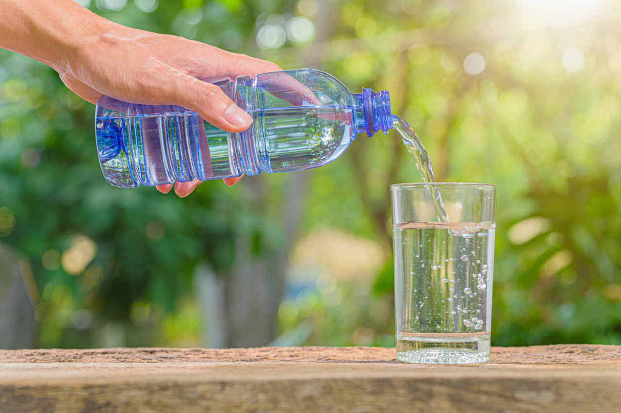 plastik şişeden cam bardağa su döken kişi