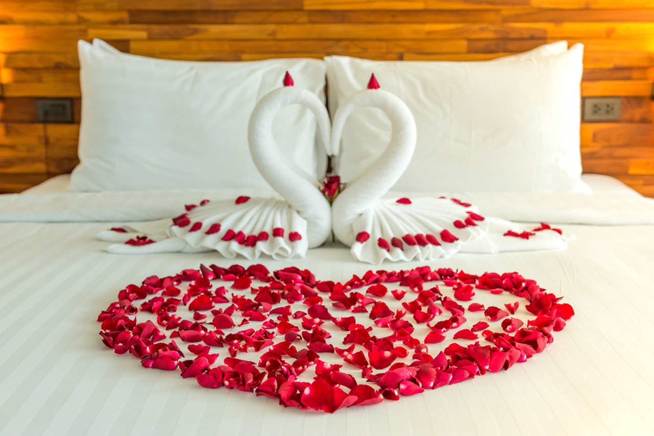 Beyaz bir yatak üzerinde kalp şeklinde kırmızı gül yaprakları