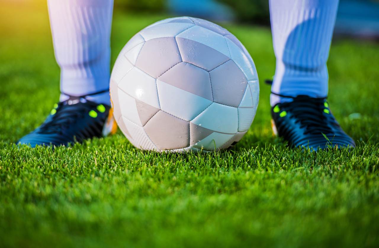 bir futbolcunun ayakkabılarının önünde duran futbol topu