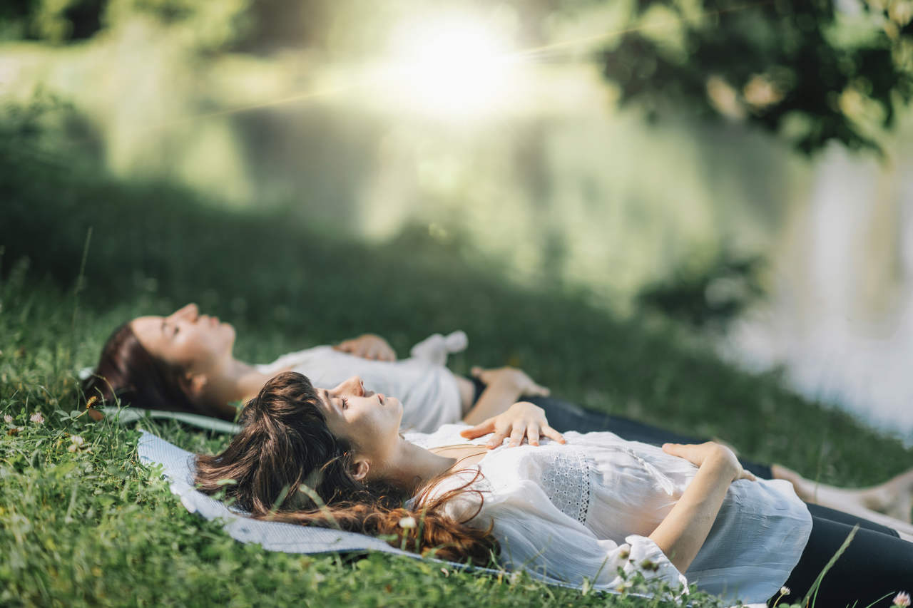çimlerin üzerinde yatarak meditasyon yapan iki kız arkadaş