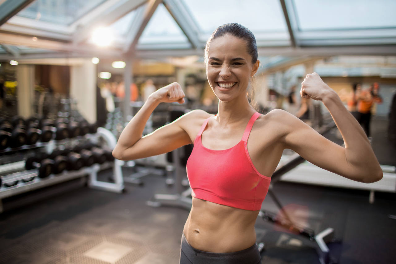 spor yapan ve kollarındaki kasları göstererek gülümseyen kadın