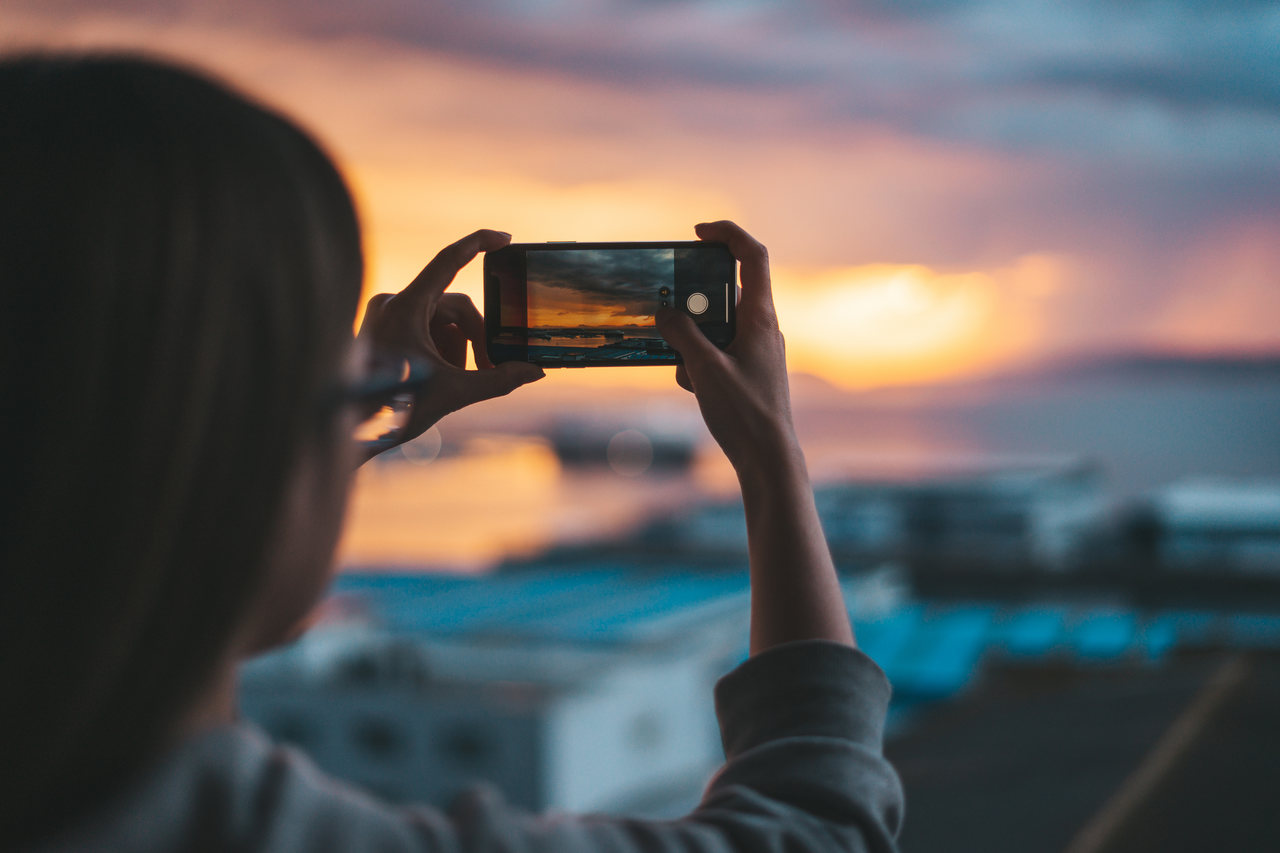 gün batımında telefon ile fotoğraf çeken kadın