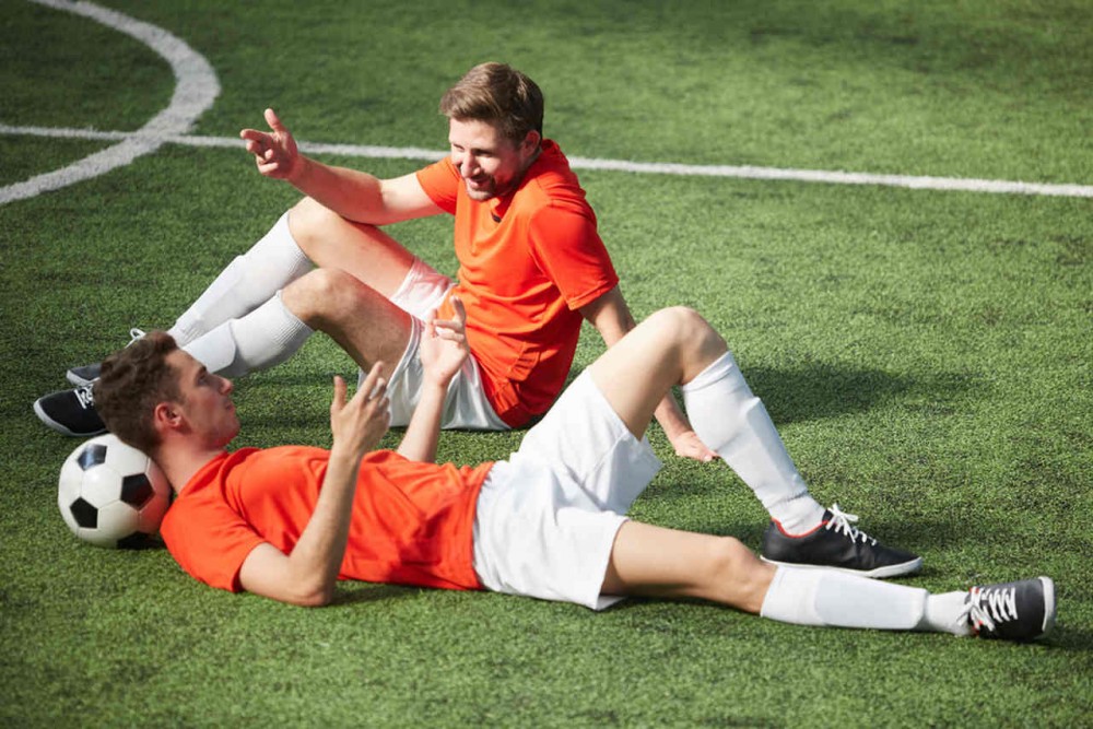 two soccer players talking and resting on the pitch