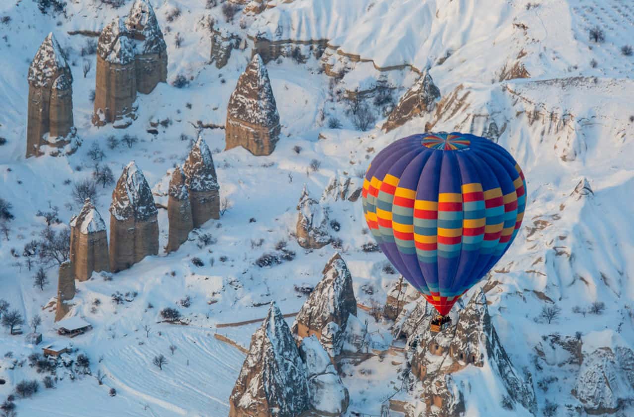 Kapadokya'da kar altında kalan peri bacalarının üzerinde süzülen renkli sıcak hava balonları
