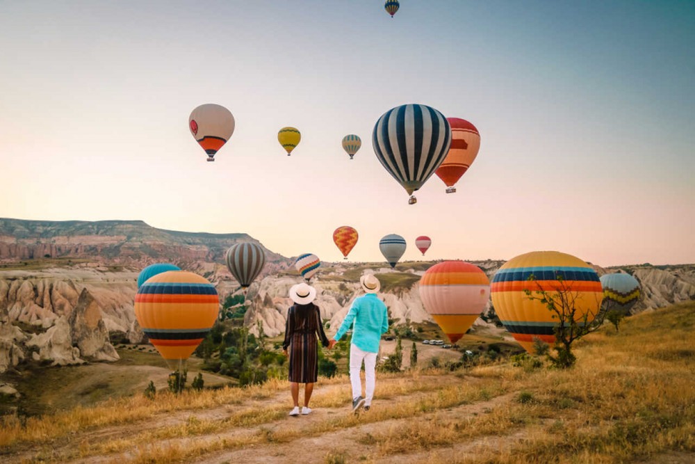 young couple looking at cappadocia and hot air balloons