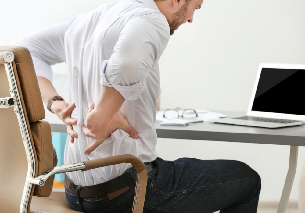 man working on a desk and holding his back