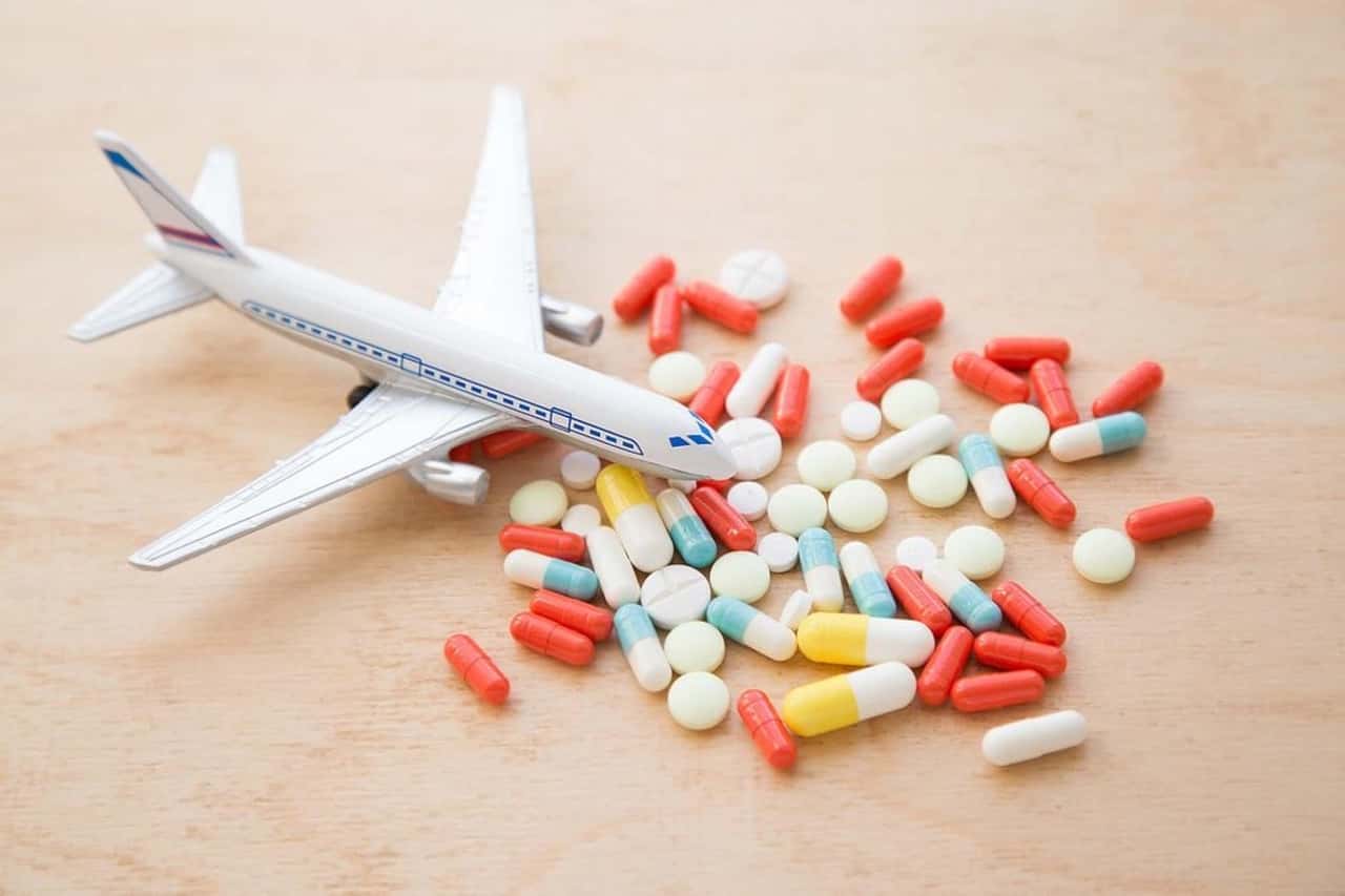 ahşap zemin üzerinde duran beyaz maket uçak ve önünde duran renkli hap ilaçlar