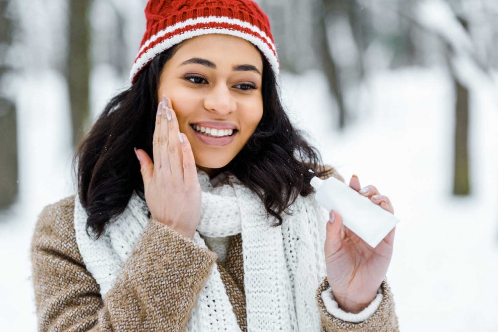 woman putting sunscreen on her face in winter